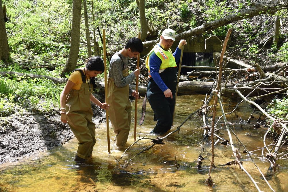 Three volunteers conduct macroinvertebrate stream sampling in 2023.

