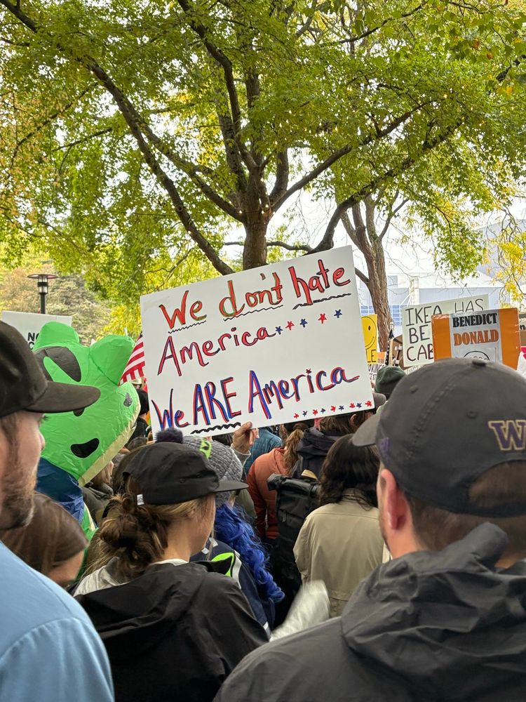 A crowd of people and a sign that says “we don’t hate America, we are America.”