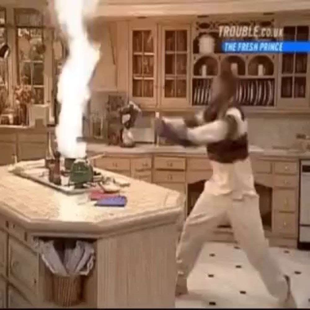 a man is standing in a kitchen with a fire coming out of the stove .