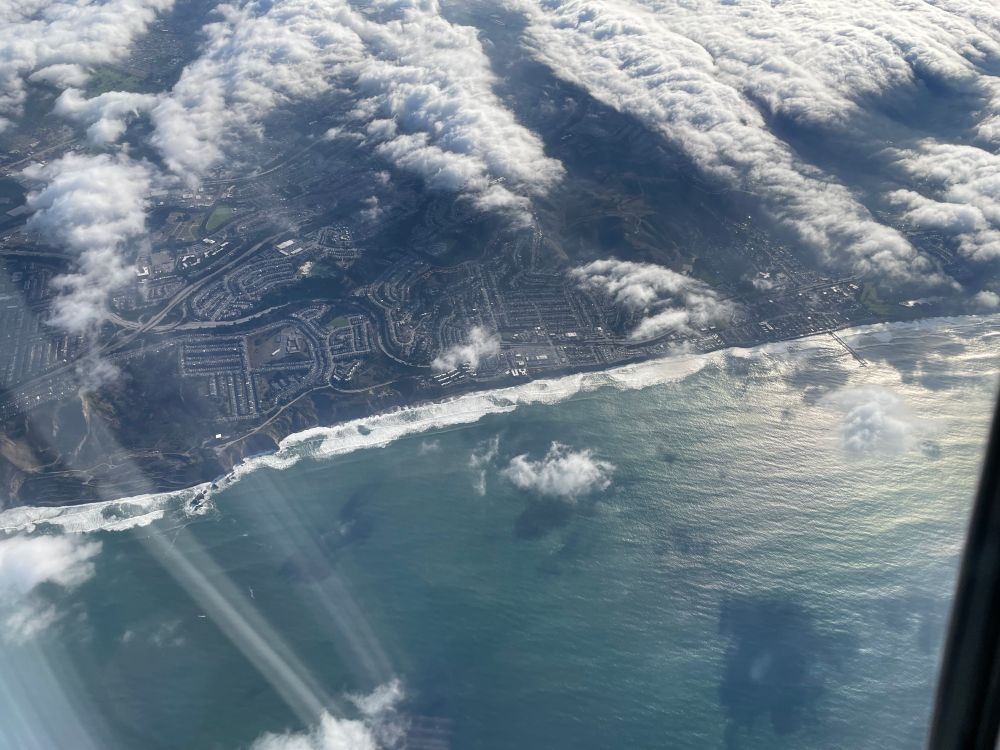 the edge of the shore and low clouds from above with a long seemingly continuous crest of waves