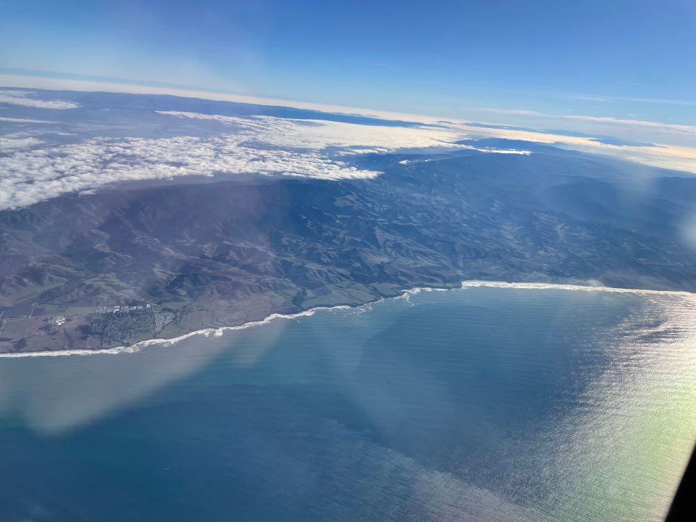 the ocean and mountains from above, with silvery light reflecting onto it.