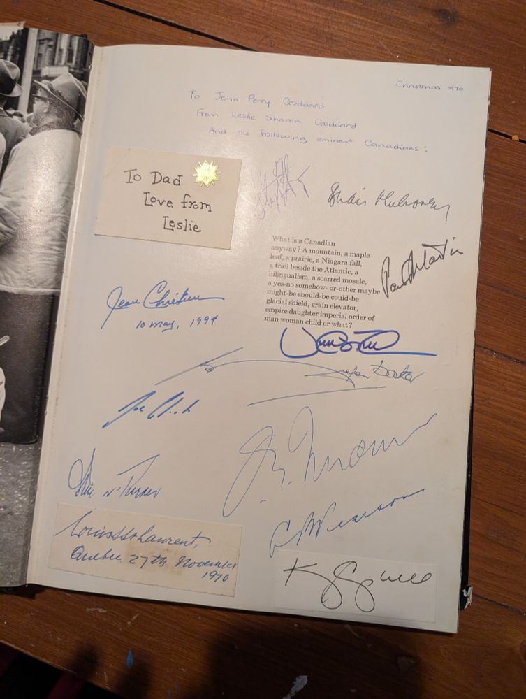 A white interior page of a book covered in signatures of different sizes and colours, there is a small piece of card attached that read 'To Dad, Love from Leslie.'