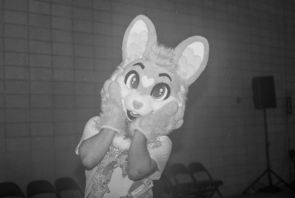 A black and white photo of my in my Sugarbun partial fursuit with my paws cupping my cheeks. Photo by Juneberry