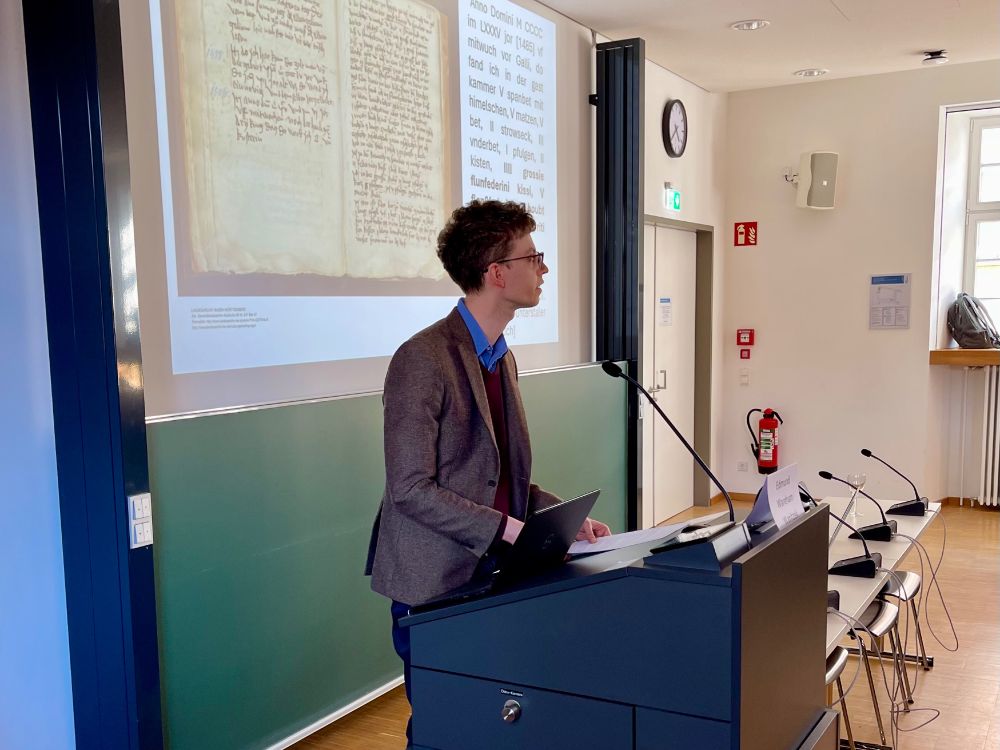 Dr Edmund Wareham Wanitzek standing at a podium with an image of a 16th-century manuscript projected behind him