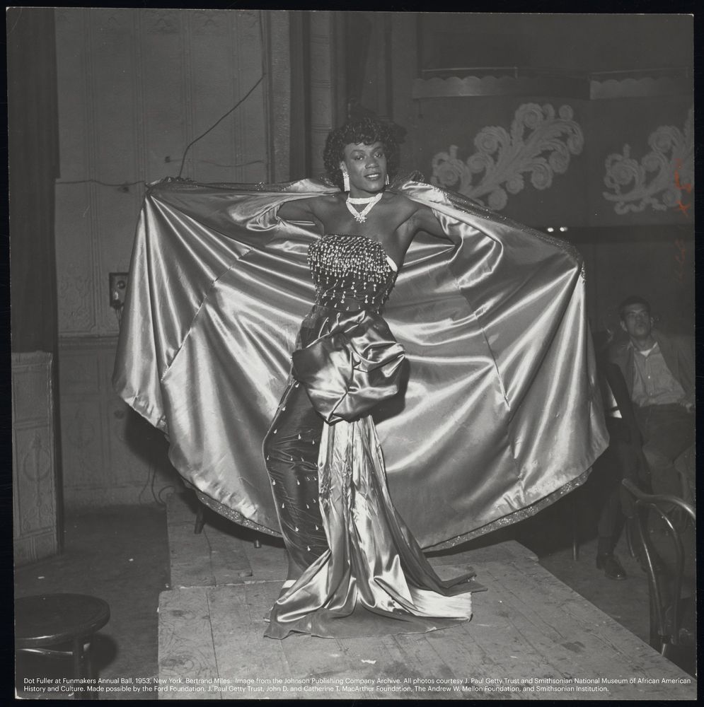 Vintage drag performer showing off their gown and cape on a stage. 