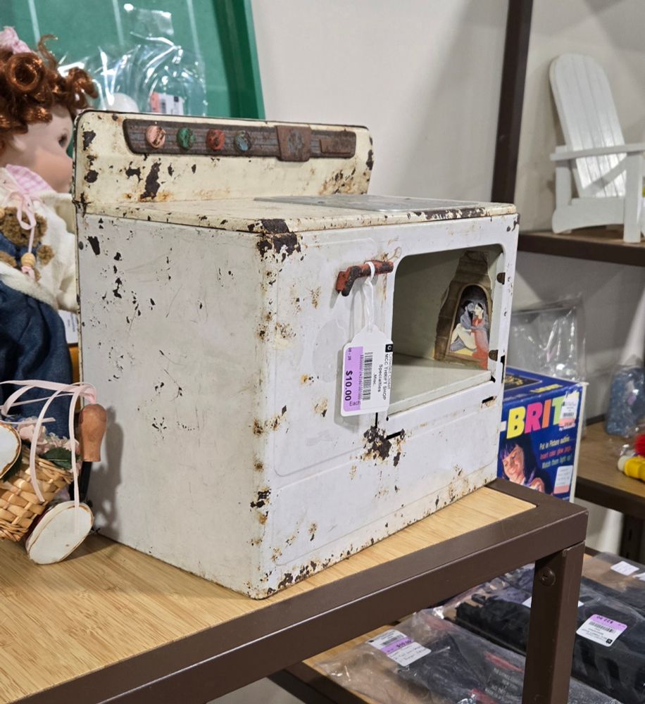 A white metal toy stove. It's slightly rusty and the door to the oven is missing. There is something painted just inside of the oven.