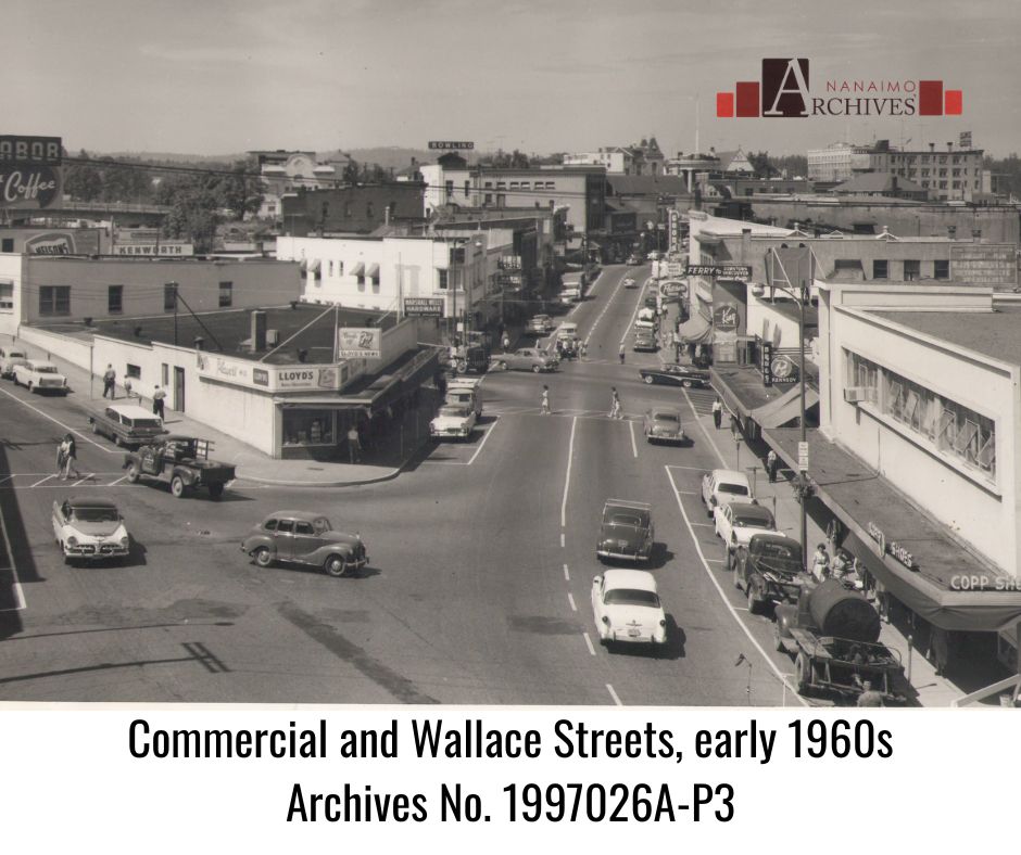 Photograph of the Wallace and Commercial Street intersection in Nanaimo around 1960.  Shows cars and buildings.