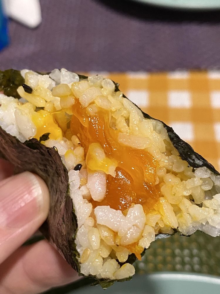 Picture of a half-eaten onigiri, showing the soy sauce-cured egg yolk filling.