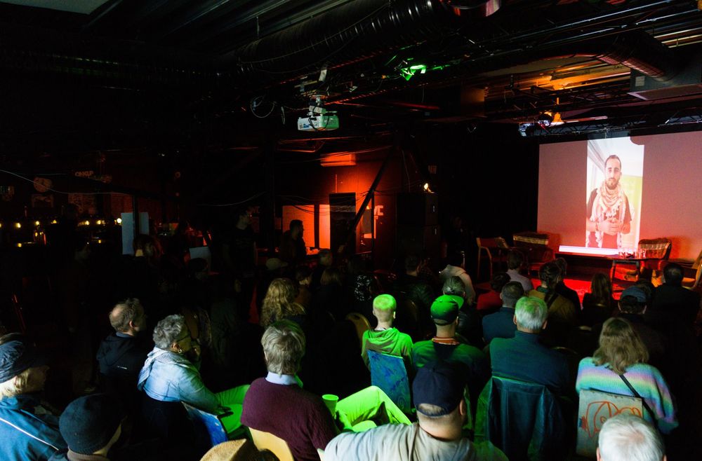 Jalal Abukhater på en skjerm, mens en fullsatt sal ser på. 