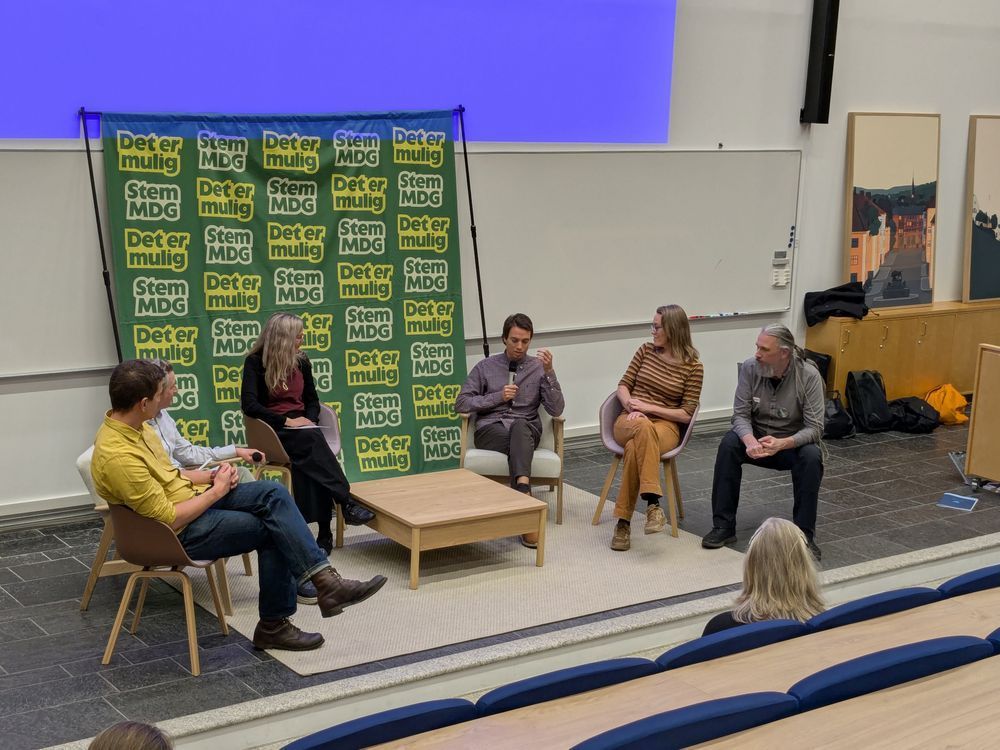 Paneldebatt med stort MDG-banner i bakgrunnen. Fra venstre ser vi Petr Vasilev, Finn Myrstad (skjult bak Petr), Maja Lunde, Philip Thingbø Mlonyeni, Christin Gorman og Johannes Brodwall