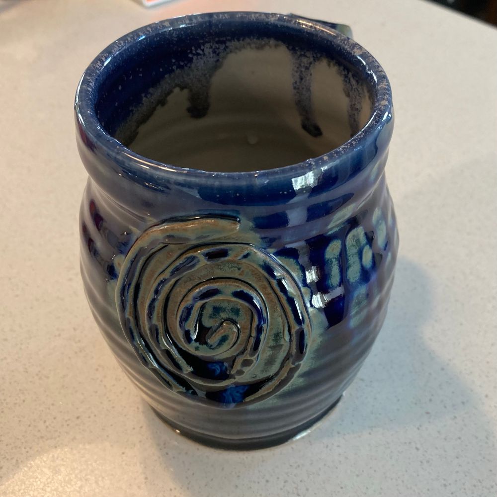 A large coffee mug, pottery style, blue and brown with a spiral pattern on one side