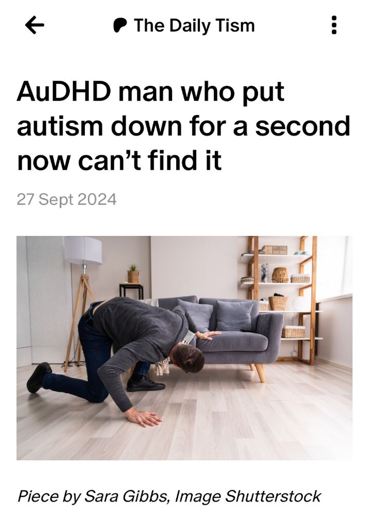 A man is crouching on the floor and looking underneath a sofa