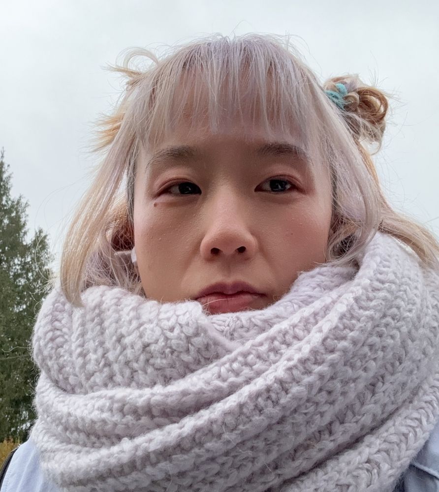 chinese feminine person with lilac knit scarf, lilac hair, under grey skies, tree in background. i am looking just off the camera and i have Nezha style hair
