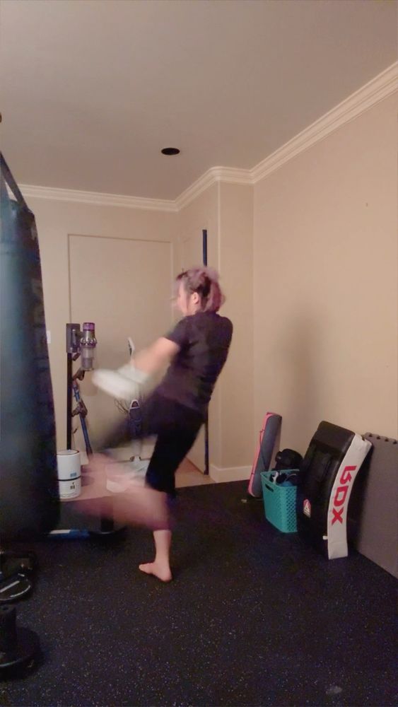 person in indoor gym mid kick at a heavy bag 