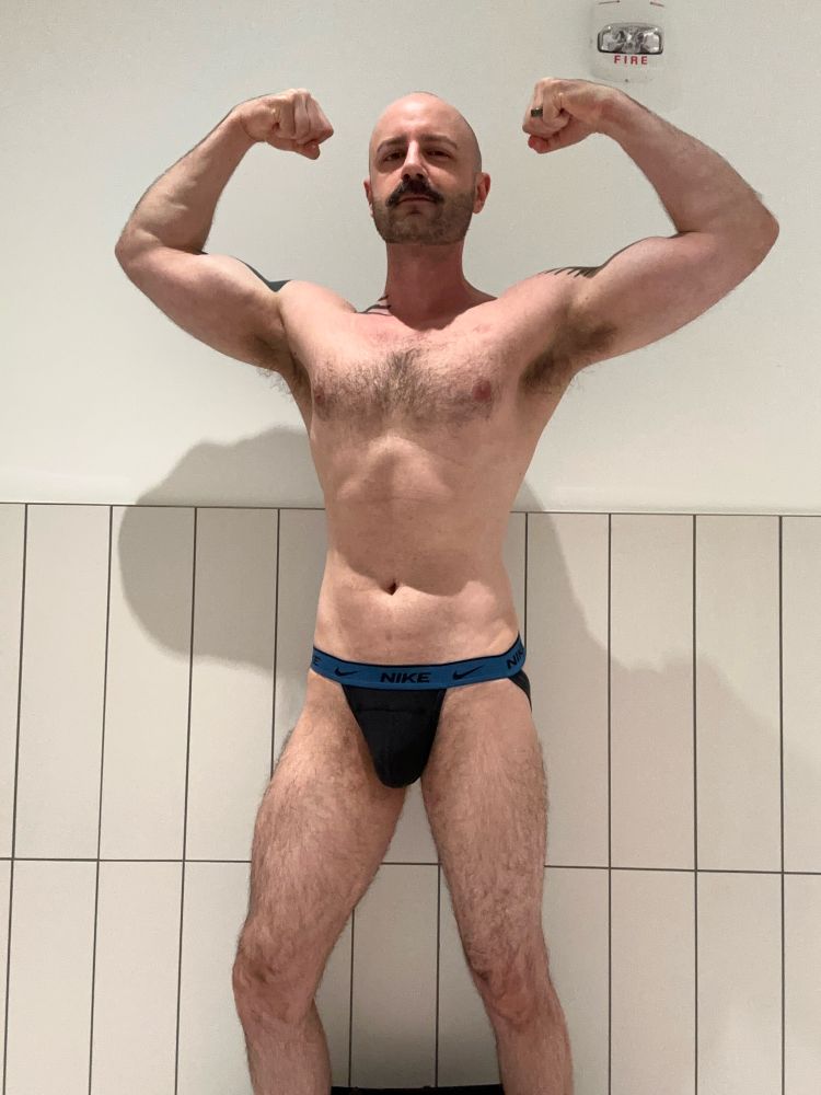 Me flexing in a restroom in a blue and black Nike jock. 
