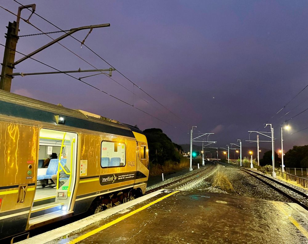 Looking north from the tip of Paremata station platform in Wellington, which has the longest history of electric trains in New Zealand. It's a drizzly winter evening but the train is bright and warm: the pic shows the front end about to head off up the line with the nearest door open. The stanchions and overhead wires for the electric power are visible along both tracks. Credit: me, 12 July 2022