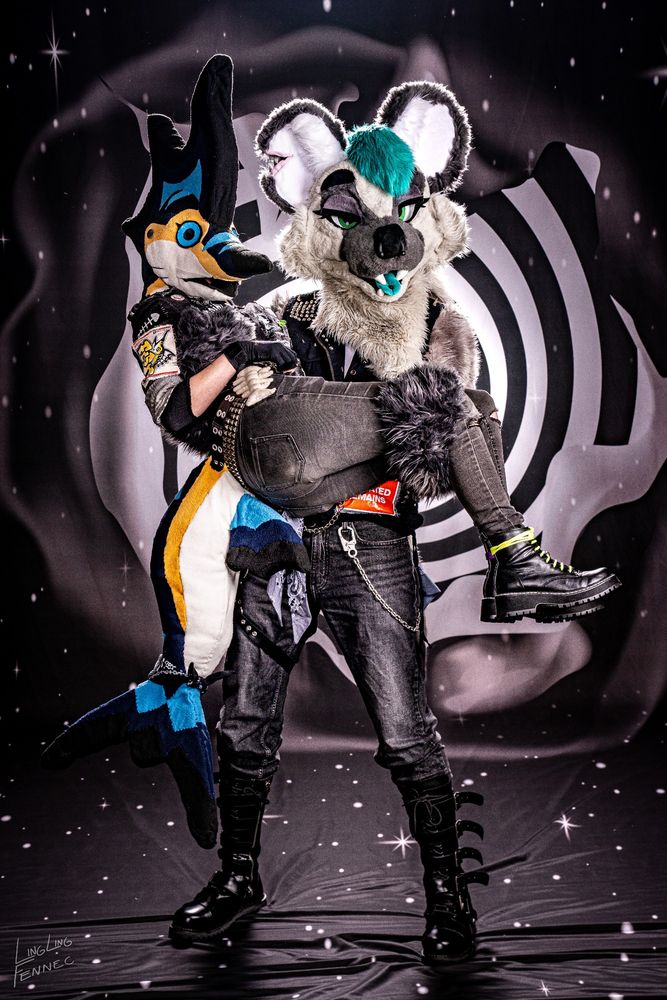 A photo of me in my hyena fursuit Harriette holding up my partner Vinny, who is wearing his Marlin Fursuit infront of a "Twilight Zone" spiral background