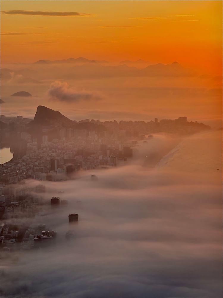 A sunrise over Rio de Janeiro, golden light breaking through thick morning fog that blankets the city’s high-rises, coastline, and mountains.