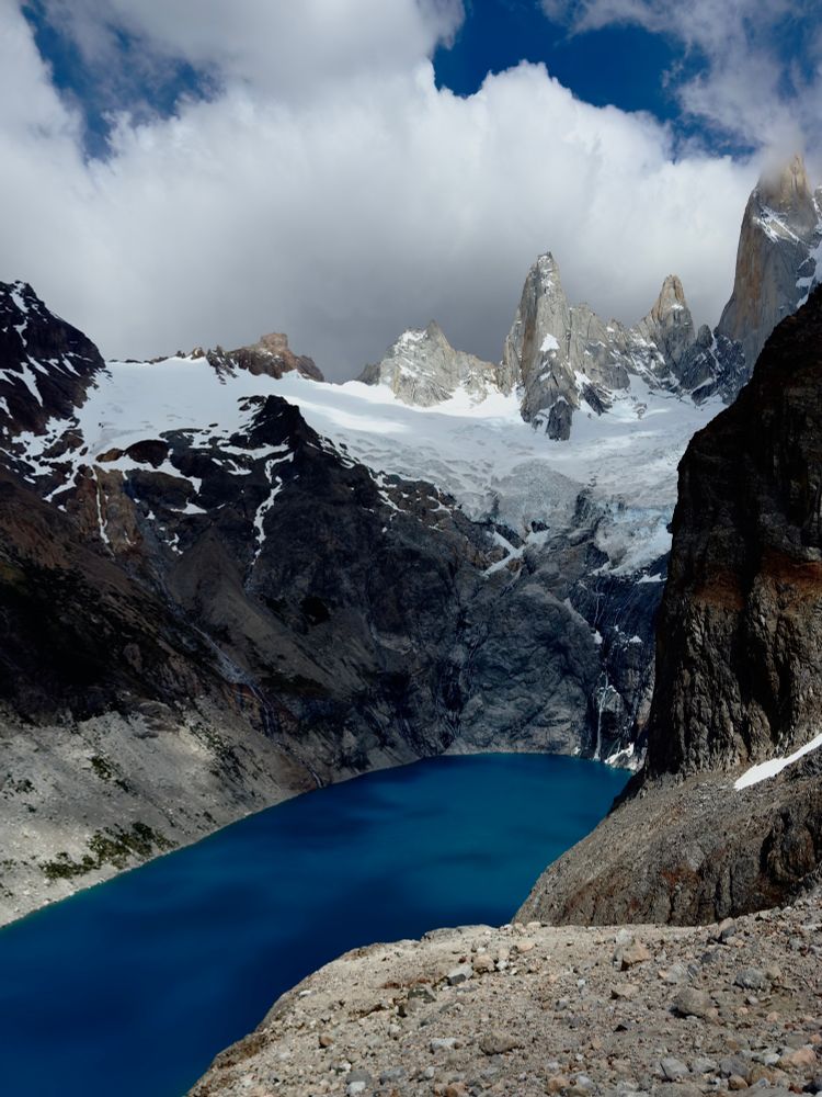Laguna Sucia, a deep blue glacial lake sits beneath dramatic snow capped peaks in Patagonia’s Los Glaciares National Park, with rocky cliffs and ice covered ridges above.