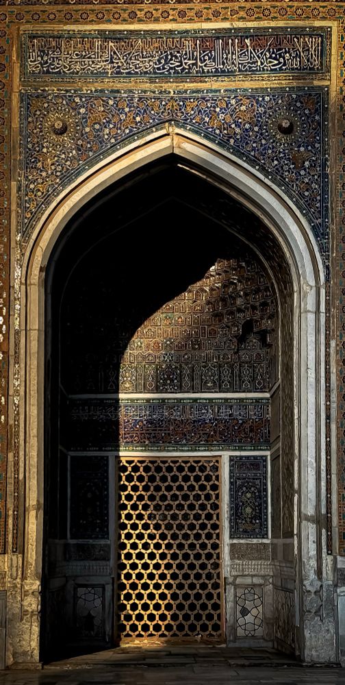 Colour photograph of an arched doorway in Samarkand’s Registan. The tiled arch bathes in half-shadow, as golden light brushes blue and turquoise tiles, turning geometry into poetry.