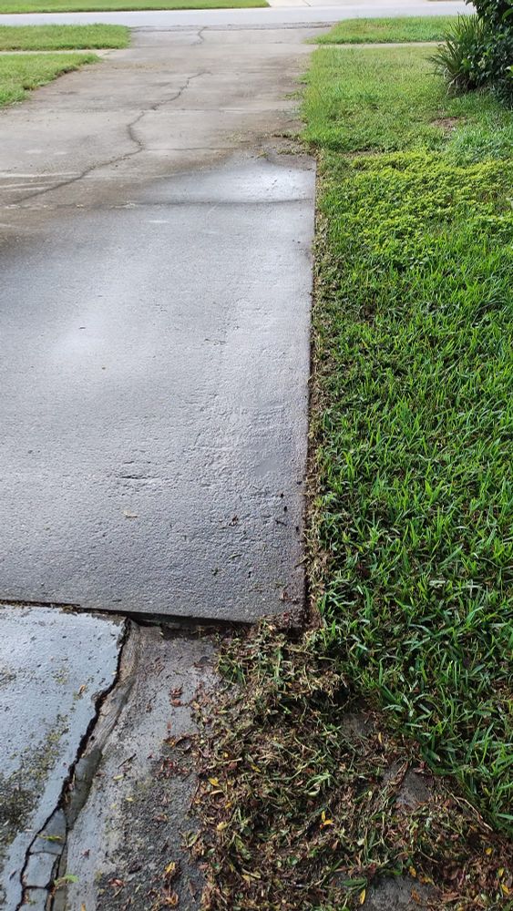 A long driveway trimmed at the edge about half way up. The edge is still covered on the other half. 