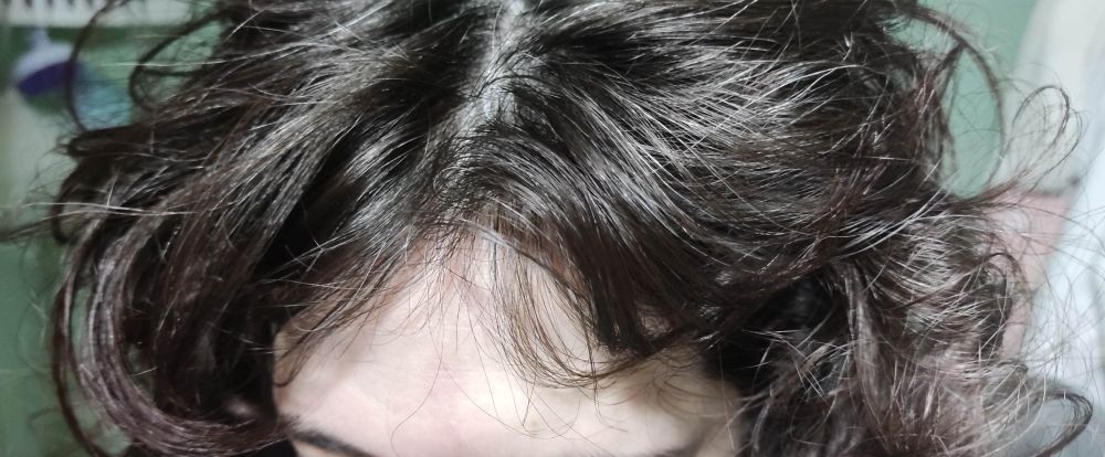 Parte superior de una cabeza con pelo oscuro y una mezcla de ondas y bucles desordenados.