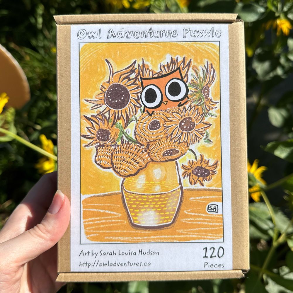 A photo of a small puzzle box showing an illustration of Owl in Vincent van Gogh's Sunflowers. The background is an out of focus patch of leafy green sunflowers.