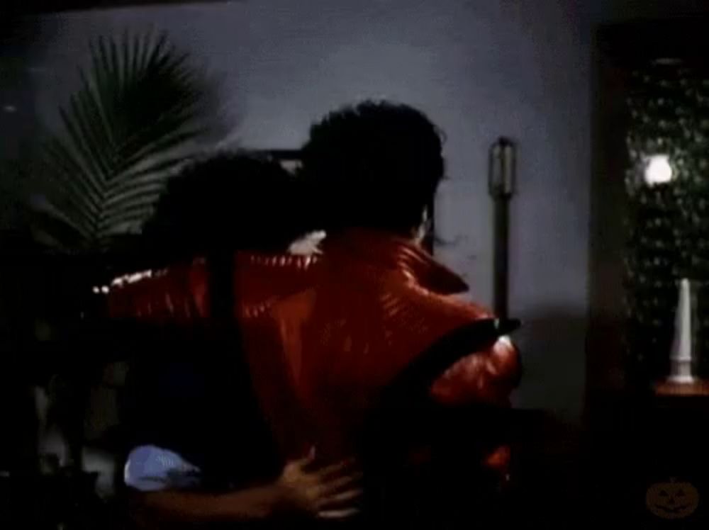 a man in a red jacket is carrying another man on his back in a living room