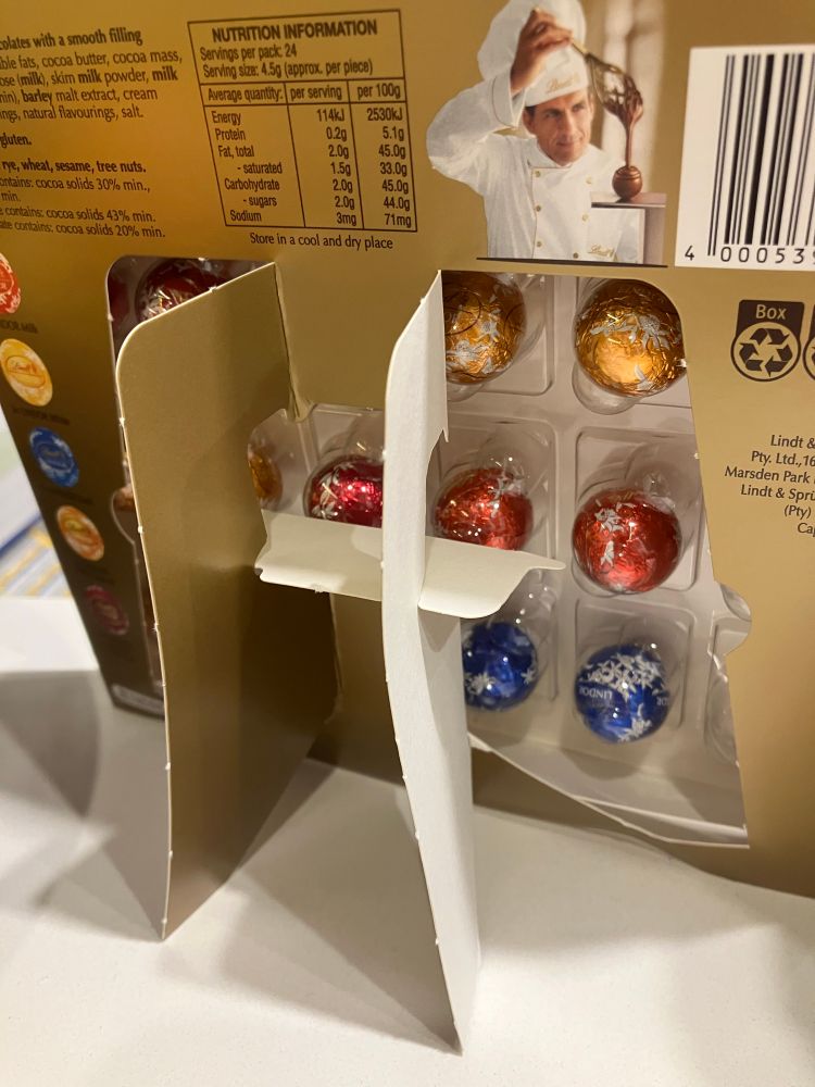 The rear side of a Lindt Lindor chocolate advent calendar. A cardboard stand has been opened up revealing clear plastic which means the chocolate behind the window is visible. 