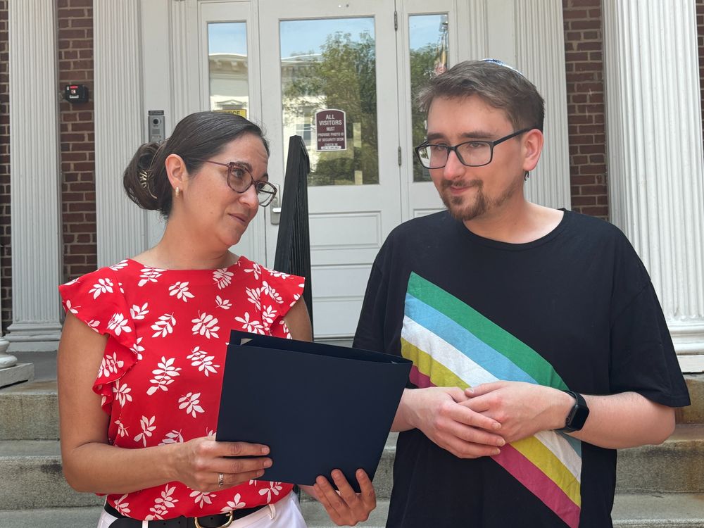 Jessica Fitzwater [left] gives a navy proclamation to Evan Evans [right], wearing a Disability Pride Flag shirt