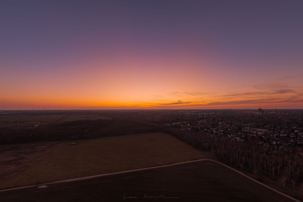 Ein farbintensives Dämmerungslicht mit orange-gelb-lila Farbverlauf bei klarem Himmel über der Landschaft bei Berlin, verursacht durch feine Partikel von polaren Stratosphärenwolken in sehr großer Höhe.