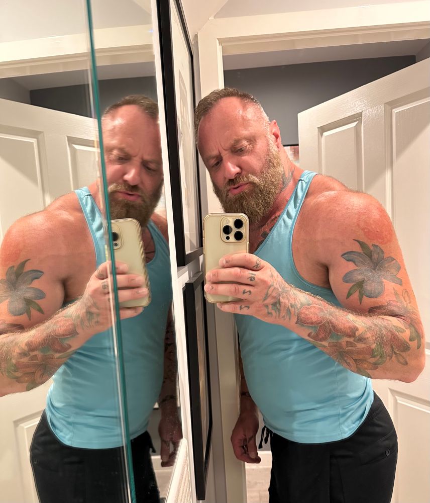 Selfie emphasising trapezius muscles with turquoise vest and black trackies bottoms 