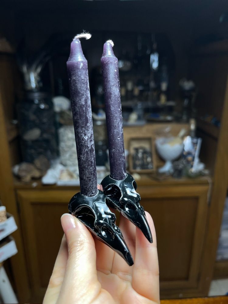 two black glazed ceramic magpie skull candle holders held in my hand. they each have a black chime candle in them
