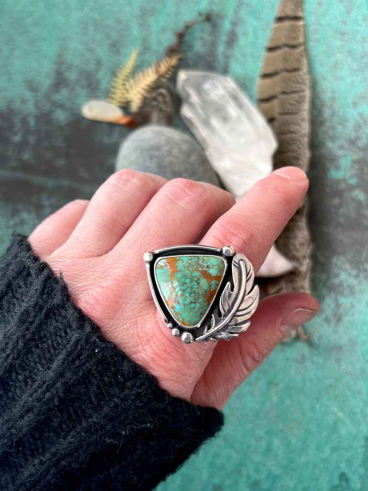 Green hue turquoise framed with a handcrafted sterling silver feather and other silver details.