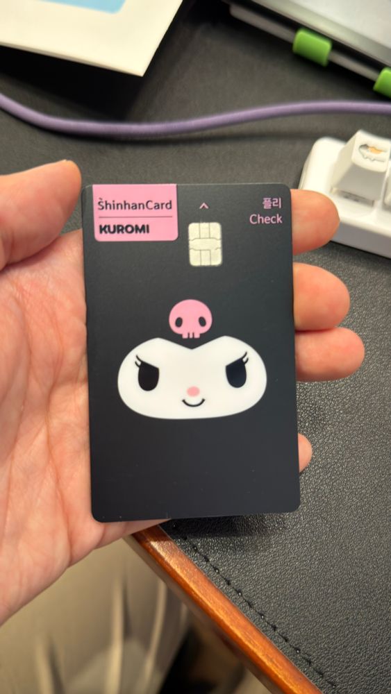 신한 체크카드에 쿠로미 라는 캐릭터의 얼굴 이미지가 그려져있다. 그 카드를 손에 들고 찍은 사진.
