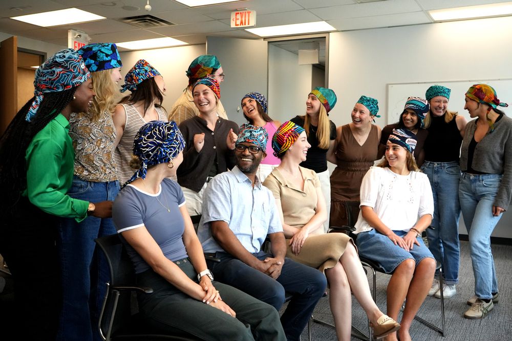 Residents wearing scrub caps, one row standing, on sitting, laughing together