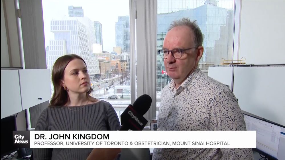 Drs. Gladstone and Kingdom speaking into reporter's microphone in front of office window
