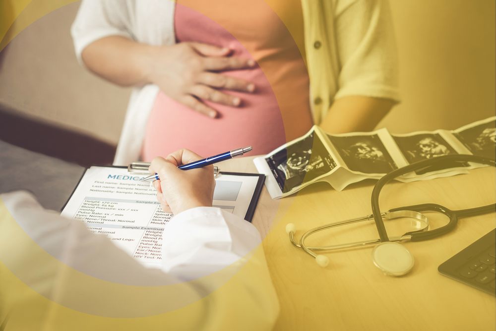 Seated doctor with clipboard talking to visibly pregnant woman
