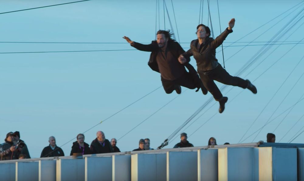This is a screenshot from the iconic jump scene in The Matrix Resurrections where Keanu Reeves and Carrie-Anne Moss leap off a 43-story building.