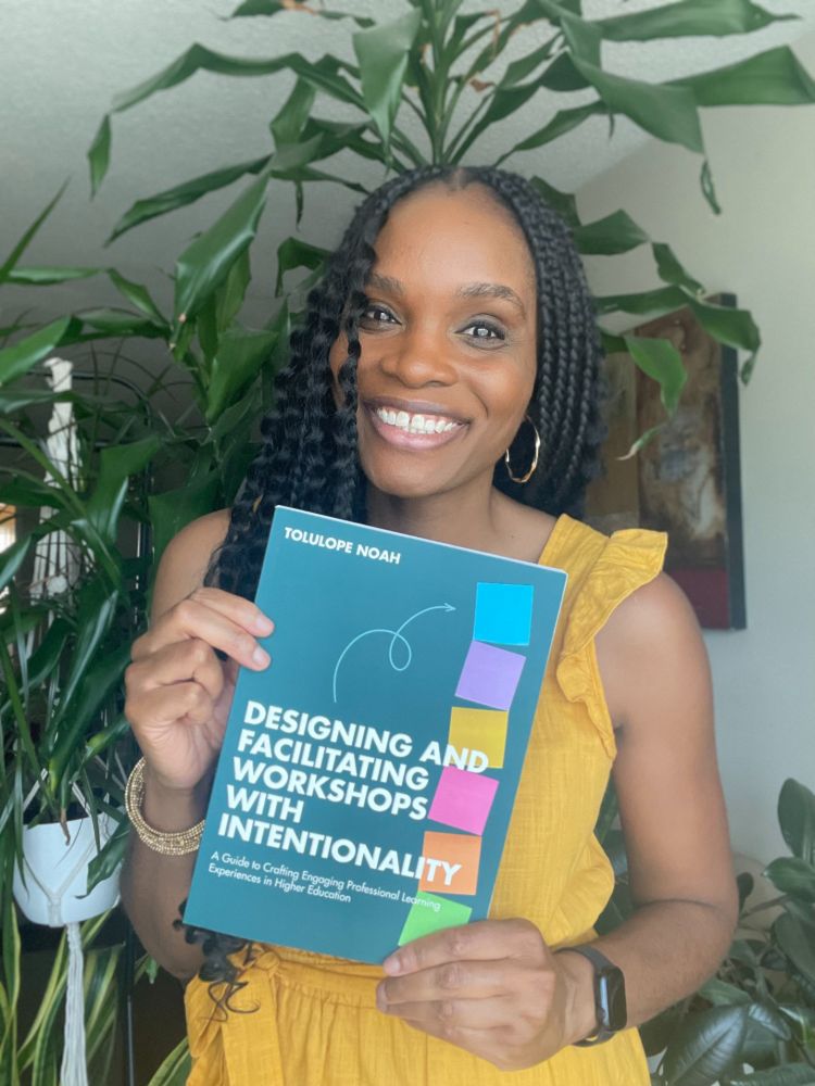 A young Black woman smiling at the camera, holding a copy of her new book, Designing and Facilitating Workshops with Intentionality.
