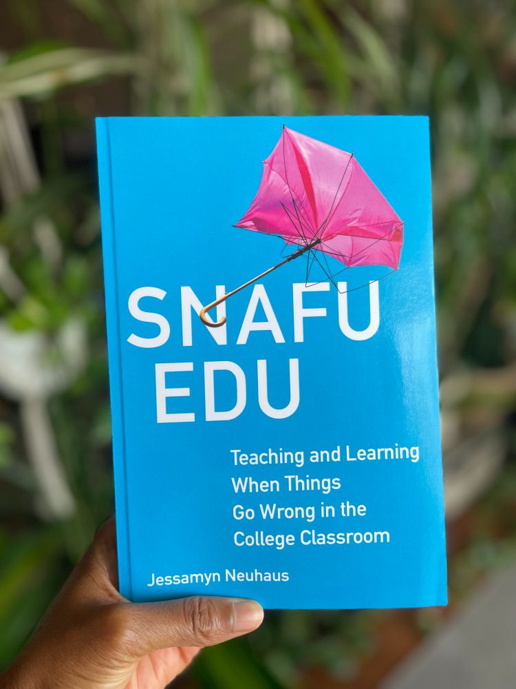 Tolu's hand holding a copy of the book, Snafu Edu, by Jessamyn Neuhaus.