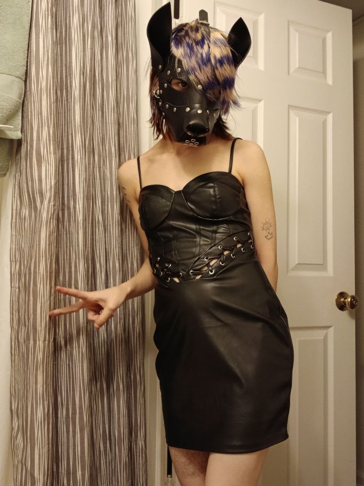 A girl wearing a leather dress and pup mask. she has blue raccoon stripes in her hair