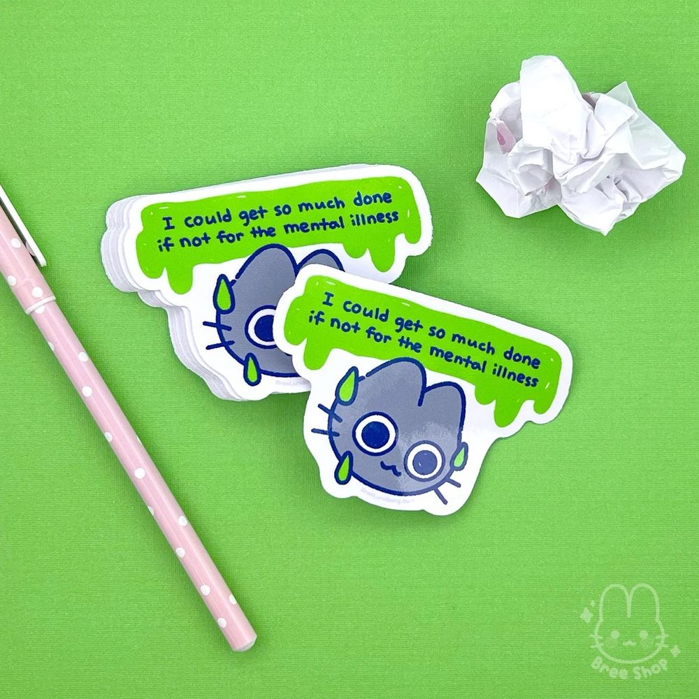 Photo of a stack of stickers of a cute illustrated grey cat's face, its eyes are wide and distressed while smiling and sweating and the words "I could get so much done if not for the mental illness" above their head in a green melting shape.