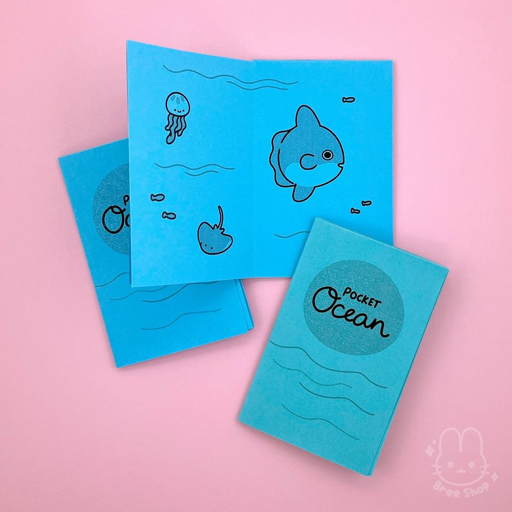 Photo of small mini zines folded out of single sheet of bright blue and teal papers, in black lettering it says “Pocket Ocean” on the cover in a circle with waves below. Another zine is open to show inside pages with cute tiny sea creatures like jellyfish, stingray, and Mola Mola (aka sunfish).