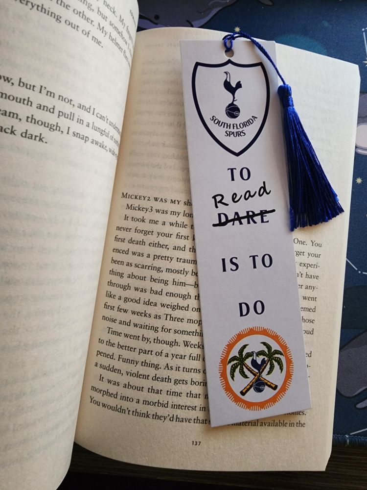 A photo of my current read: Mickey7. My South Florida Spurs bookmark is on page 137. It says "To Dare is to Do" but has the word Dare crossed off and says "read". Therefore saying "To Read is to Do" 