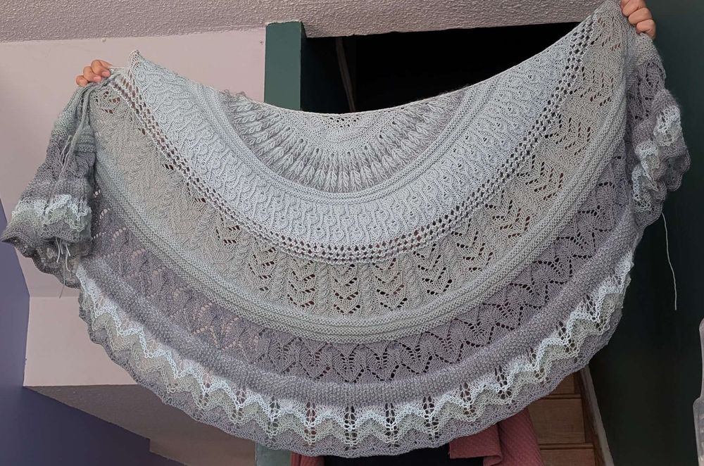 A hand-knitted blue-grey shawl, with sections of lace and cables
