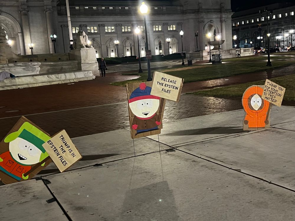 Signs with South Park characters themselves holding signs that say Trump is in the Epstein files, release the Epstein files, thank you for your attention to this matter with union station in the background 