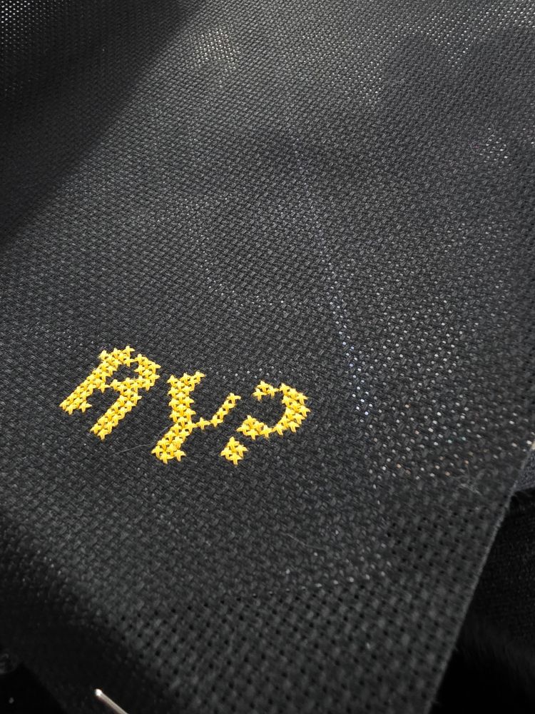 Cross stitched "RY?" in gold on black fabric. 