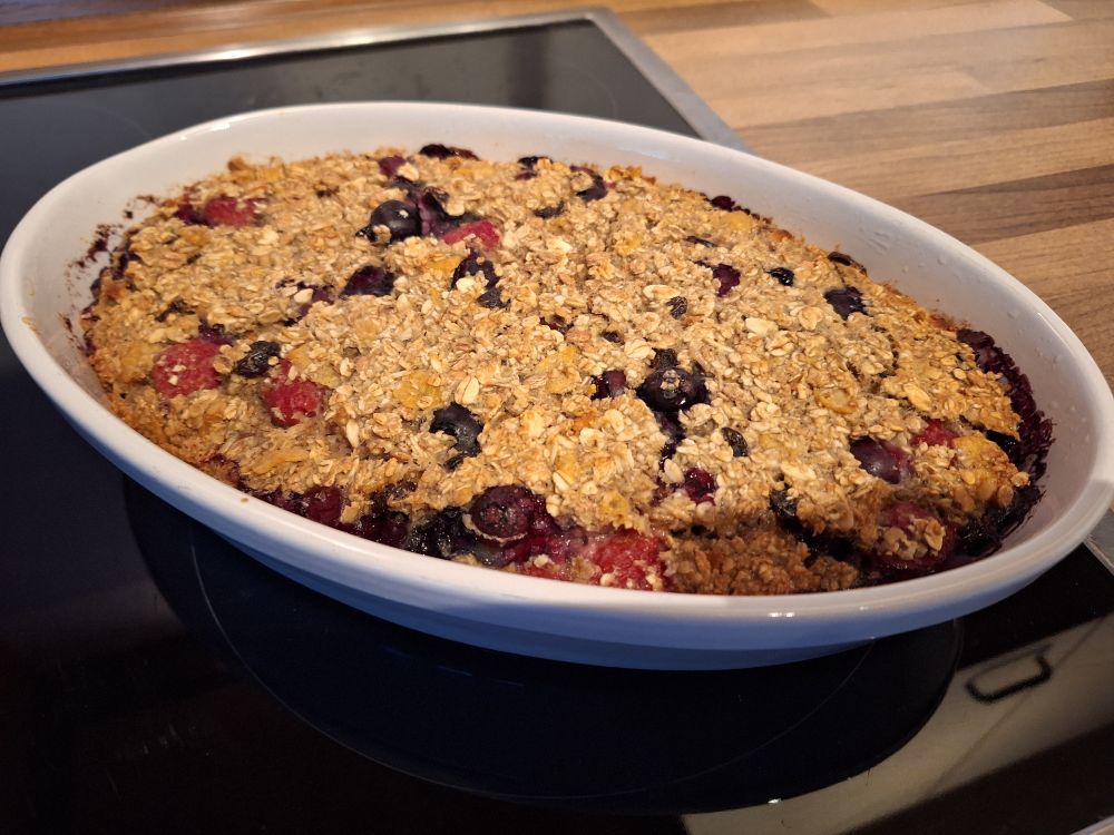 Haferflocken Kuchen mit Früchten in einer weißen ovalen Keramikform auf dem Ceranfeld stehend