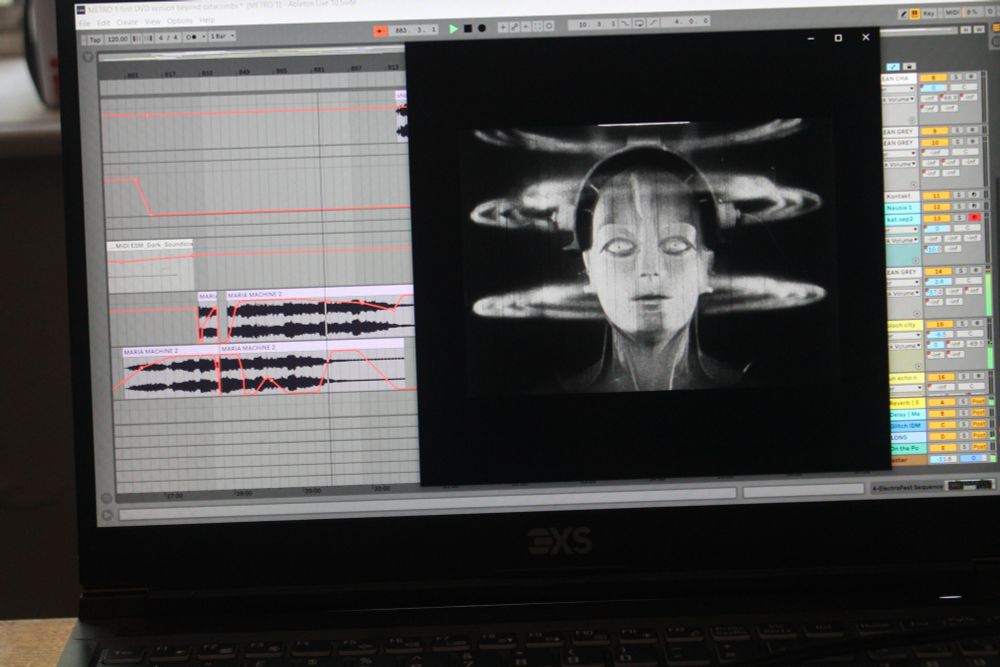 A computer screen with a samll box showing a still from the film Metropolis and Ableton music software behind with music wave forms